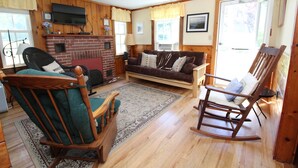A cozy living room with a fireplace, wooden walls, a sofa, a rocking chair, and a television.