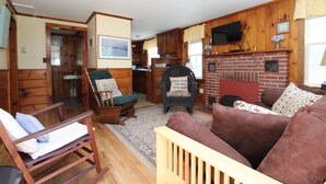A log cabin interior with a fireplace, wooden furniture, and a television mounted above it.
