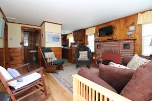 A log cabin interior with a fireplace, wooden furniture, and a television mounted above it.