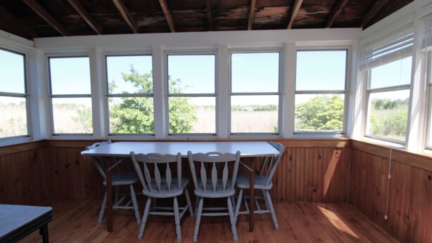 A room with a wooden table and chairs, large windows, and a view of the outdoors.