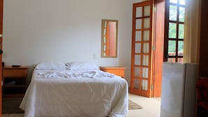 Un dormitorio con cama, mesita de noche, cómoda, espejo y puerta que da a un balcón.