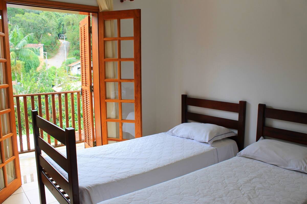 Een slaapkamer met twee bedden, een balkon en uitzicht op groen.