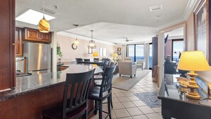 A modern kitchen with a central island, dining area with chairs, and a living room with a sofa and a lamp. - Fantastic Rates! Gulf Front 3Br/2Ba*12th Floor*Phoenix X Unit 1213 (Orange Beach)