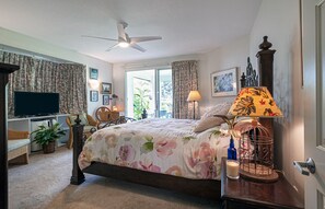 A bedroom with a bed, a ceiling fan, a TV, a lamp, and a window with curtains. - Air-conditioned, spacious, golf-front living with great long-stay rates! (Princeville)