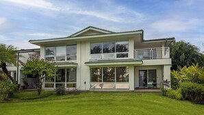 A two-story house with a balcony, large windows, and a well-maintained lawn. - Air-conditioned, spacious, golf-front living (Princeville)