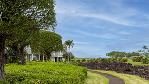 A landscaped garden with a pathway leading to a building, surrounded by trees and greenery. - Air-conditioned, spacious, golf-front living (Princeville)