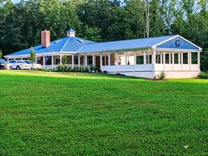 A large, single-story building with a blue roof and a white exterior. It has a covered patio area with multiple windows and a flagpole.