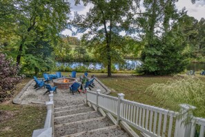 A stone staircase leading to a fire pit area surrounded by blue chairs, with a lake and trees in the background.