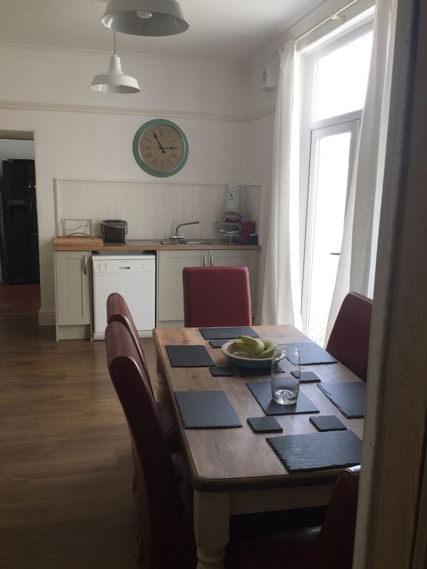 A dining area with a wooden table, red chairs, a bowl of fruit, and a clock on the wall. - Yazelle town house (Llanelli)