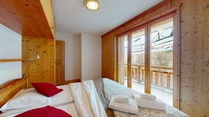 A bedroom with a bed, a red pillow, a wooden ceiling, a window, and a balcony with a view of the outside.