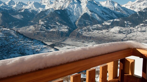 A snow-covered mountain landscape with a wooden balcony railing.