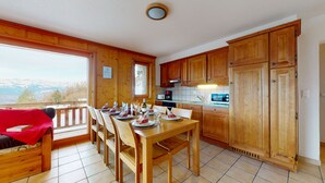 A wooden interior with a dining table set for four, wooden cabinets, and a view of mountains through a window.