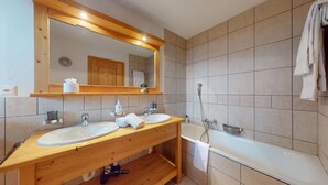 A modern bathroom with two sinks, a large mirror, and a bathtub.