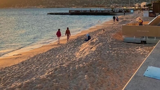 A beach with people walking and sitting, a pier in the background, and a clear sky. - 2 ROOMS, IN LUXURY RESIDENCE, SWIMMING POOL, AIR CONDITIONING, BY THE SEA (Antibes)