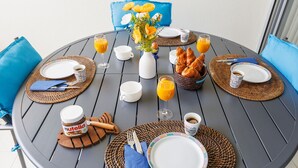 A round table set for breakfast with plates, cups, and a basket of croissants. - 2 ROOMS, IN LUXURY RESIDENCE, SWIMMING POOL, AIR CONDITIONING, BY THE SEA (Antibes)
