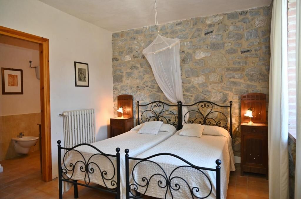 Un lit double à baldaquin, un mur en pierre, un radiateur et une table de chevet avec une lampe.