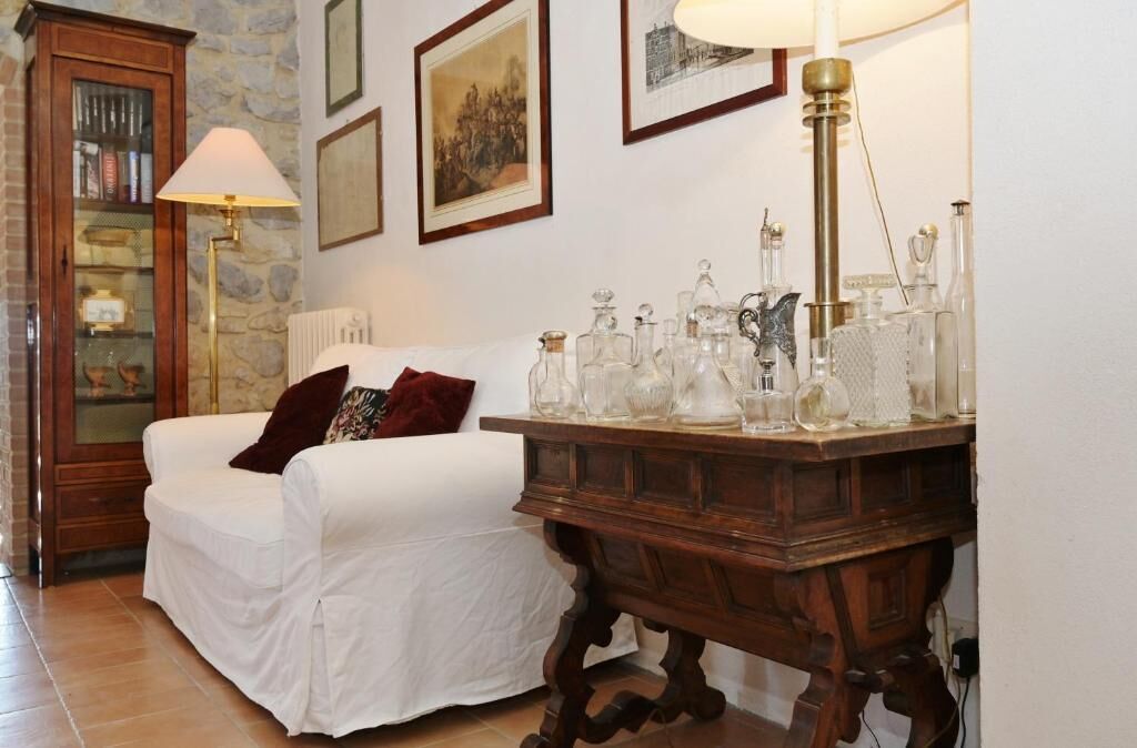 A cozy room with a white sofa, a wooden side table with glassware, a lamp, and framed pictures on the wall.