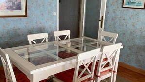 A dining area with a glass-top table and white chairs with red cushions.