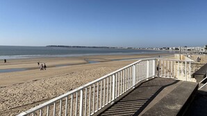 A beach with a white railing, sandy shore, and a clear blue sky.