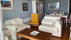 A living room with two white sofas, a yellow armchair, a wooden coffee table, and a cabinet with glass doors.