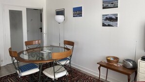 Un comedor con una mesa redonda de vidrio, cuatro sillas, una lámpara de pie y una mesita con una cesta y un radio.