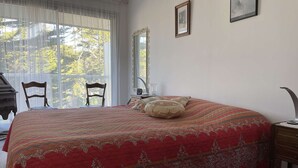 Un dormitorio con una cama grande, una silla, un escritorio y una ventana con cortinas.