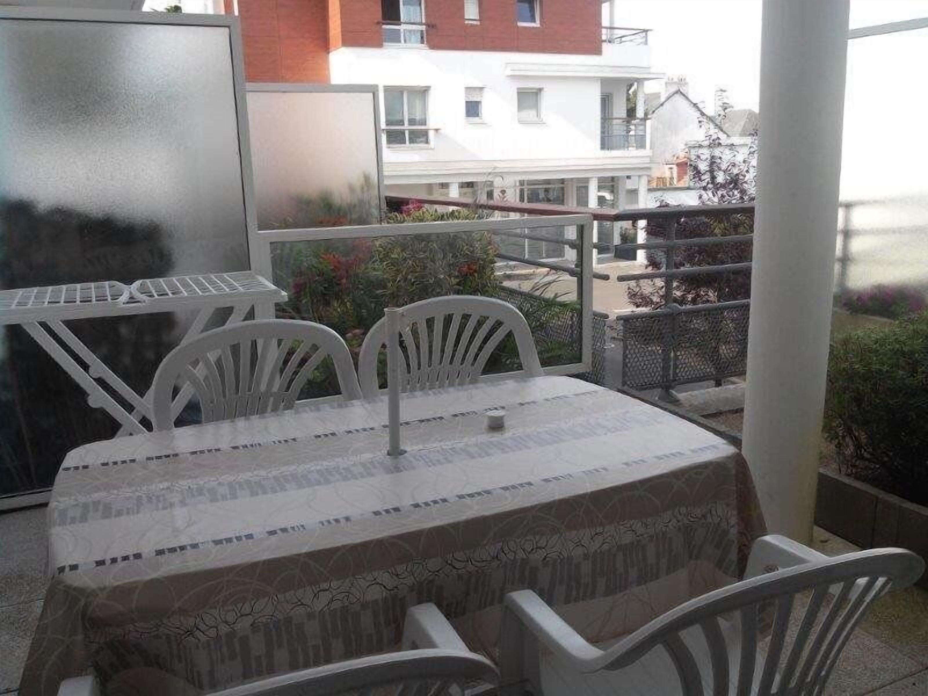 Un balcon avec une table et des chaises, une porte vitrée et une vue sur les bâtiments en arrière-plan.
