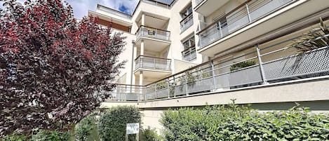 Een meerlaags woongebouw met balkons, een tuin met een bord en een boom met rode bladeren.