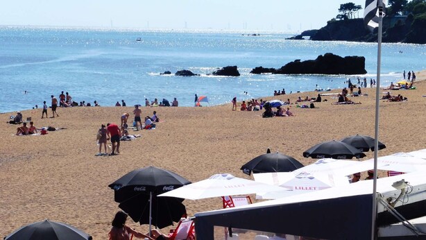 Une plage avec des parasols, des tables et des gens.
