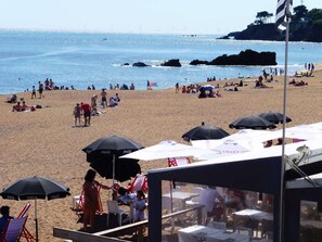 A beach with umbrellas, tables, and people. - Saint Marc SUR MER 2 Pièces Centre-ville (SAINT MARC SUR MER)