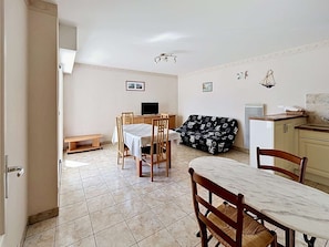 A dining area with a table and chairs, a sofa, a small bench, and a kitchenette.