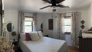 A bedroom with a bed, a ceiling fan, two windows with curtains, a bedside table, a mirror, and a dresser. - Mountain retreat with close proximity to lake and town square (Prescott)