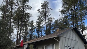 A single-story house with a stone foundation and a sloped roof, surrounded by tall pine trees. - Mountain retreat with close proximity to lake and town square (Prescott)
