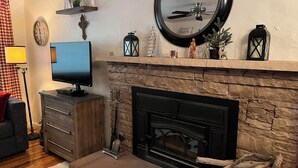 A living room with a stone fireplace, a television on a wooden cabinet, and decorative items on the mantel. - Mountain retreat with close proximity to lake and town square (Prescott)