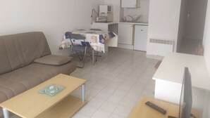 Ein kompakter Wohnbereich mit Sofa, Esstisch, Küchenzeile und Fernseher.