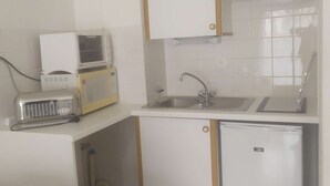 Eine kompakte Küche mit weißen Schränken, einer eingebauten Mikrowelle, einem Spülbecken und einem kleinen Kühlschrank.