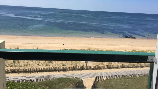 A beach view from a window with a wooden fence and a clear sky.