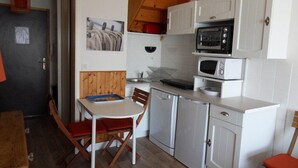 A compact kitchen with white cabinets, a microwave, a stove, and a sink. There is a dining table with chairs and a small window above the sink.