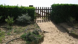 A sandy pathway leading to a wooden gate, flanked by neatly trimmed hedges.