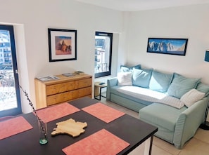 A living room with a sofa, a wooden cabinet, a table with placemats, and two framed pictures on the wall.