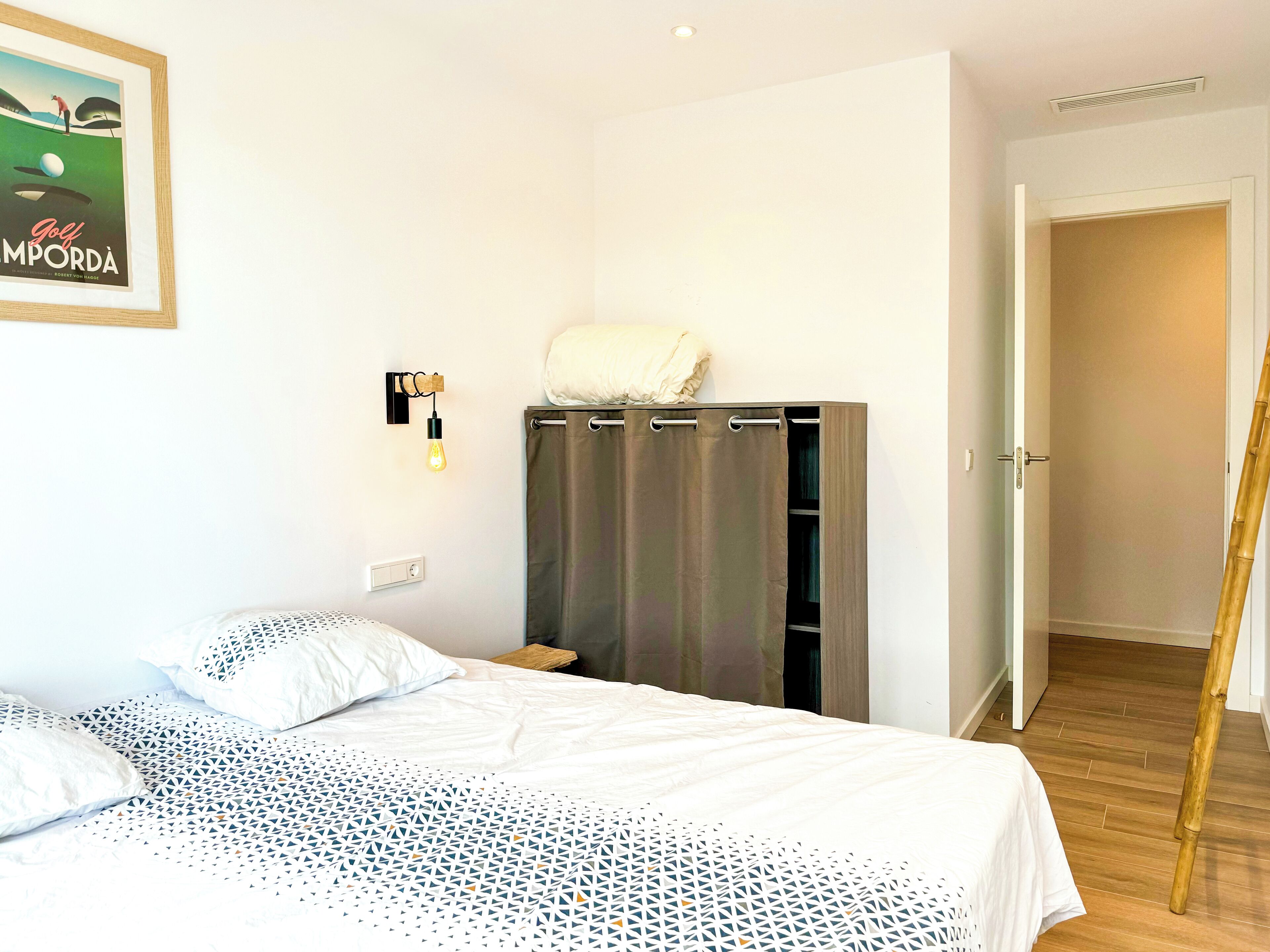 Un dormitorio con cama, armario, lámpara y una puerta que da a otra habitación.