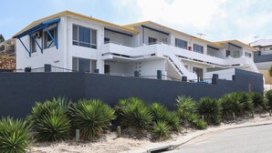 Un edificio moderno de dos pisos con fachada blanca, detalles en azul y un muro gris al frente.