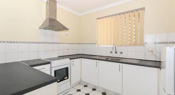A kitchen with white cabinets, a black countertop, a stove, a sink, and a window with blinds. - THE Tide Scarborough (Perth)