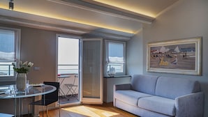 A modern living room with a grey sofa, a glass dining table, and a painting of a seaside scene. - Attico Vista Mare sul Porticciolo di Camogli by Wonderful Italy (Camogli)