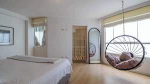 Un dormitorio con cama, una silla colgante, una ventana y una puerta.