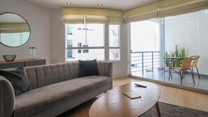 Una sala de estar moderna con sofá, una mesa de centro y un comedor con sillas. Hay un ventanal que ofrece vistas al exterior.