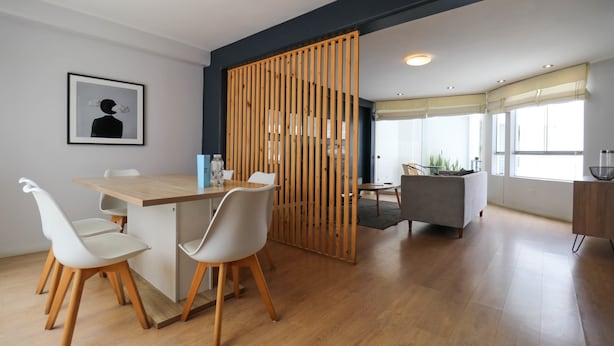 Un comedor moderno con una mesa de madera y sillas blancas, un separador de madera y vistas a una zona de cocina.