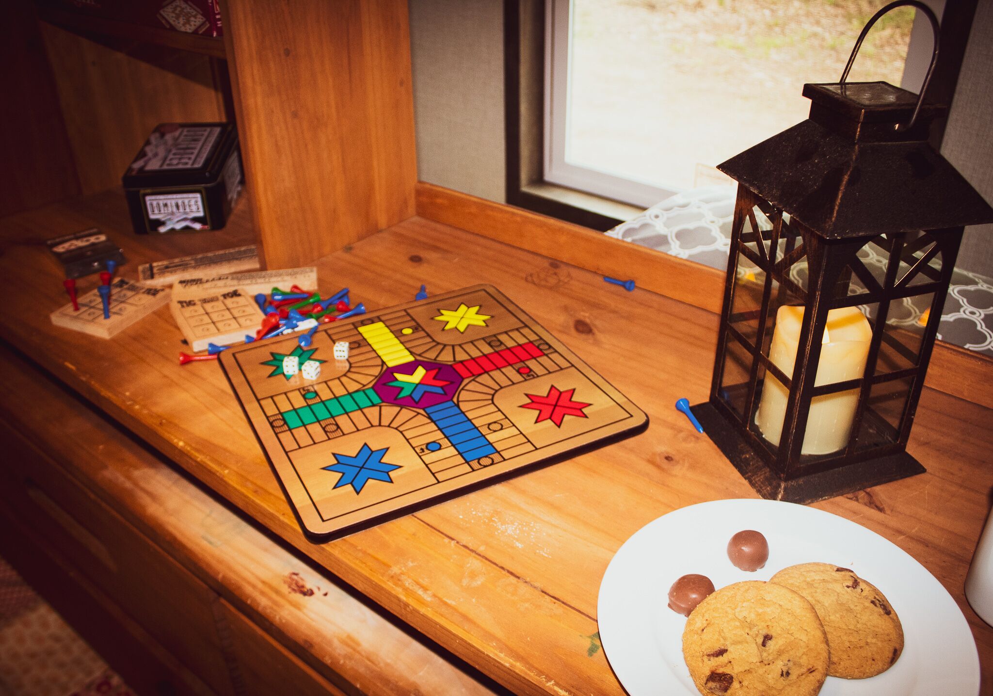 Una mesa de madera con un juego de mesa, una vela y un plato de galletas.