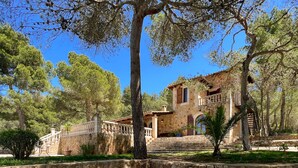 Una villa in pietra con una scala in pietra che conduce a una porta di legno, circondata da alberi e un muro in pietra.