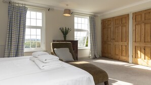 Une chambre à coucher avec un grand lit, une chaise, une armoire en bois et une fenêtre avec des rideaux.